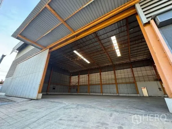 Warehouse for rent or sale in Mueang Samut Sakhon, Samut Sakhon - Open steel sliding doors revealing a high-clear warehouse with skylights and a wide concrete loading apron.