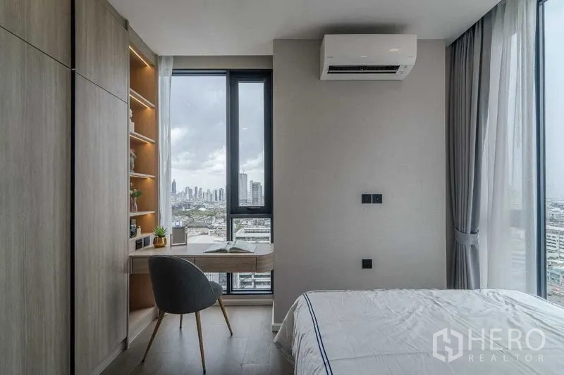 Condominium for rent in Pathum Wan, Bangkok - Bedroom study nook with built-in shelves and desk by tall windows facing the skyline.