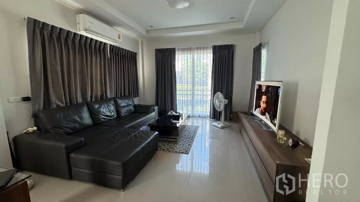Detached House for sale in Lat Krabang, Bangkok - Bright living room with black leather sectional sofa, TV cabinet, tiled floors and sliding doors to the garden.