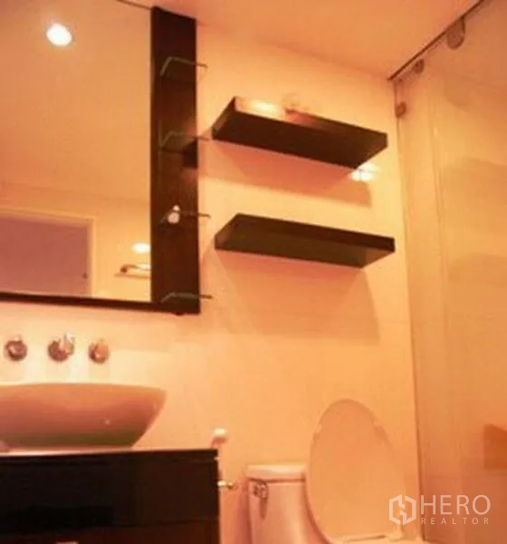 Condominium for rent in Pathum Wan, Bangkok - Modern bathroom with a vessel sink, wall shelves, toilet and a glass-enclosed shower.