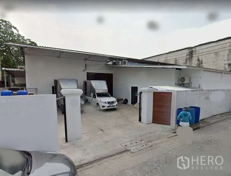 คลังสินค้า ให้เช่าหรือขายในMin Buri, Bangkok - ด้านหน้าโกดังชั้นเดียวสีขาวย่านมีนบุรี พร้อมประตูม้วน ลานคอนกรีต และที่จอดรถขนส่ง
