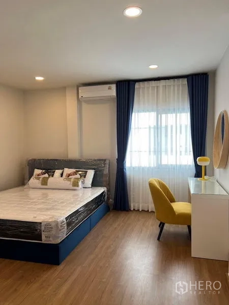 独立式住宅 出租在Bang Phli, Samut Prakan - 次卧配大床，蓝色窗帘与带黄色椅子的学习桌。