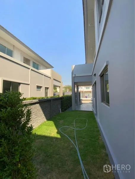 Detached House for rent - Narrow side garden with hedge, lawn, and garden hose along the house.
