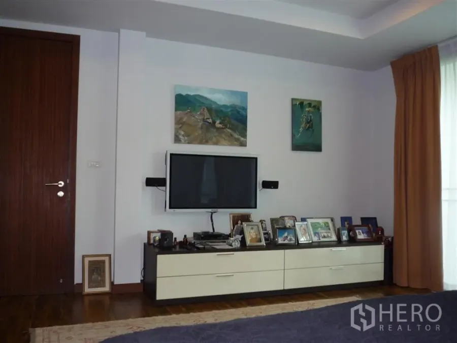 Detached House for rent in Khan Na Yao, Bangkok - Media wall with mounted TV, low console and framed photos on wood flooring.