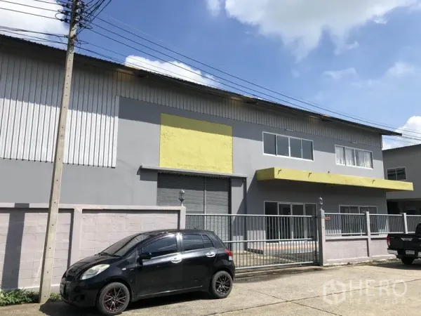 Factory for rent in Pathum Thani - Two-storey factory facade with grey walls, yellow awnings, metal gate and parking in Lat Lum Kaeo.