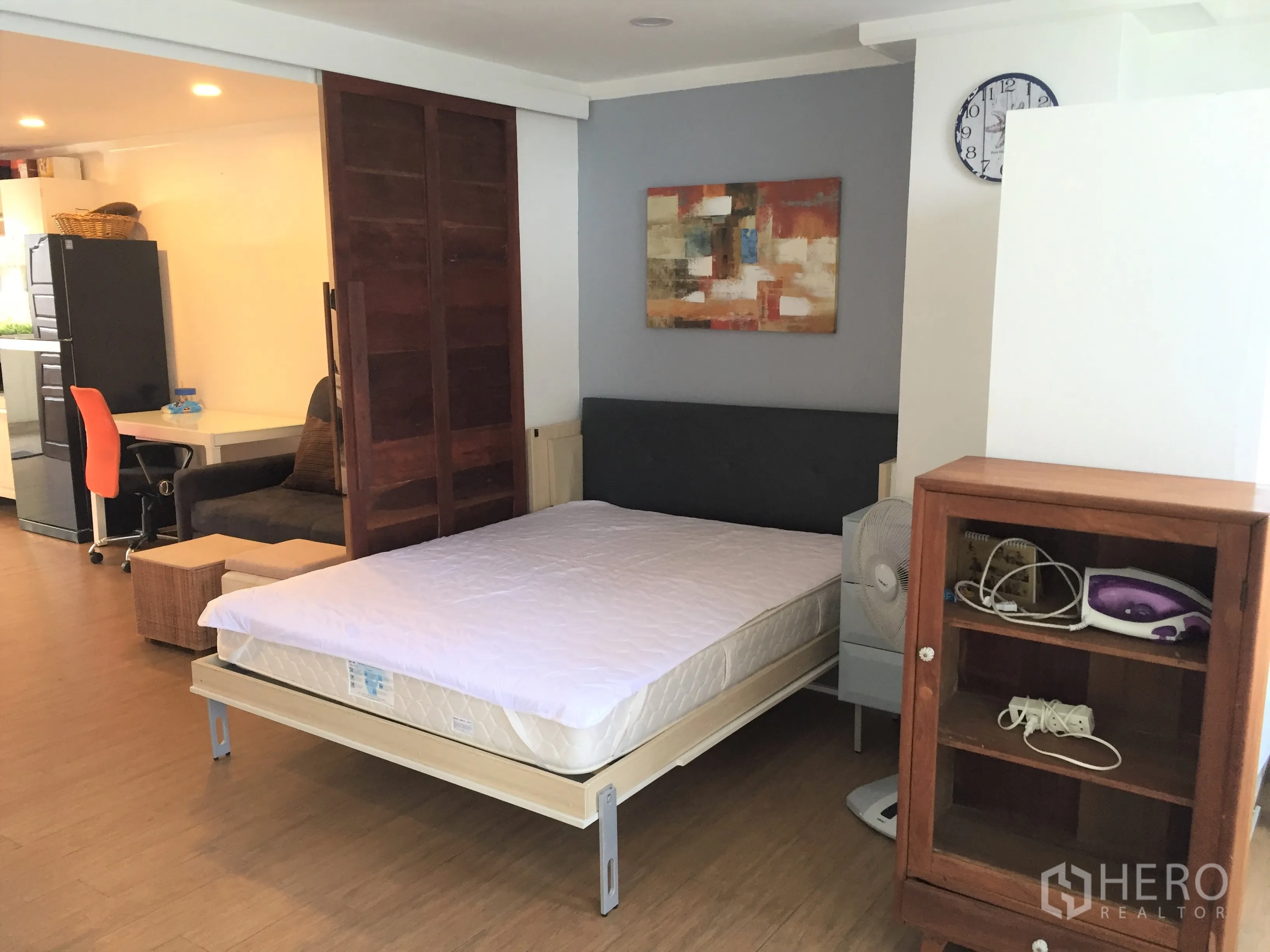 Condominium for rent in Watthana, Bangkok - Bedroom area with wood floors, sliding wooden door, desk, and shelving beside the bed.