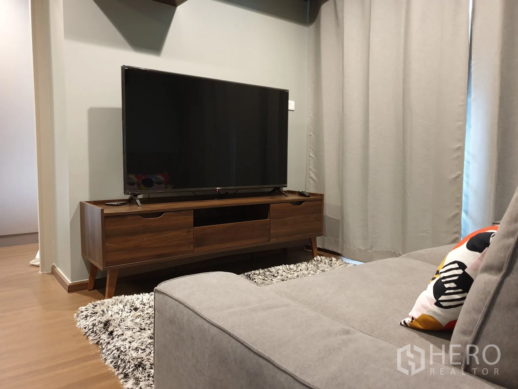 公寓 for rent in Phra Khanong, Bangkok - 客厅配灰色沙发、木质电视柜与落地窗帘。