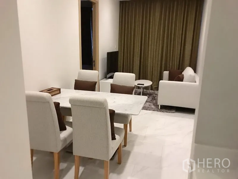 Condominium for rent in Watthana, Bangkok - Open‑plan dining and living space with marble‑top table, upholstered chairs, sofa set, TV and full‑height curtains.