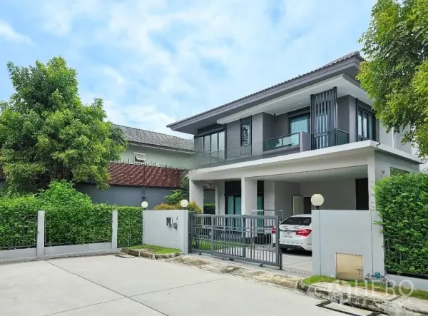 Detached House for sale in Lam Luk Ka, Pathum Thani - Angled exterior of the two-storey home with covered parking and landscaped hedges on a quiet street.