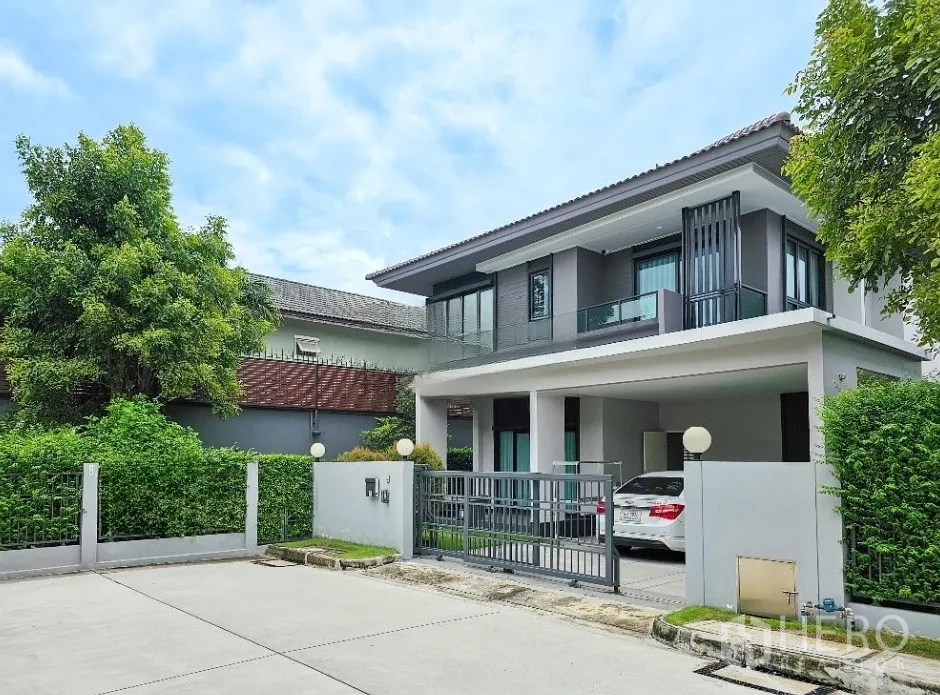 Detached House for sale in Lam Luk Ka, Pathum Thani - Angled exterior of the two-storey home with covered parking and landscaped hedges on a quiet street.