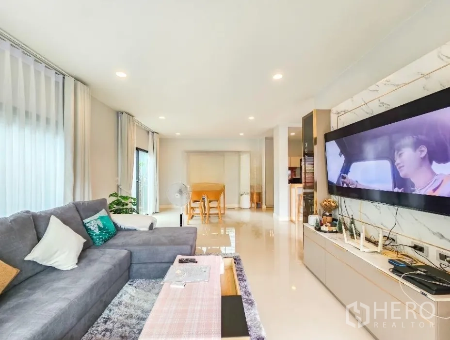 Detached House for sale in Lam Luk Ka, Pathum Thani - Open-plan lounge featuring a wall-mounted widescreen TV and glossy tiled floors.