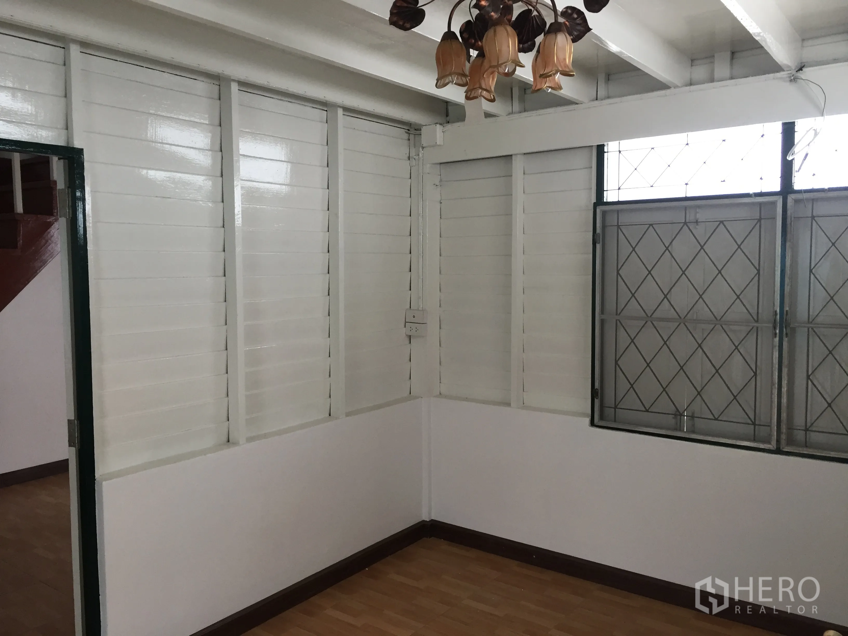 บ้าน ให้เช่าในBang Rak, Bangkok - ห้องนั่งเล่นโทนขาว ผนังบานเกล็ด พื้นไม้ หน้าต่างเหล็กดัด และโคมไฟแขวน