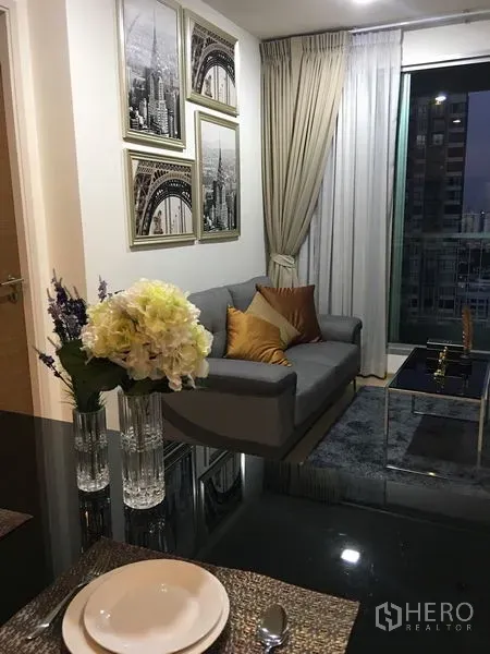 公寓 出租在Khlong Toei, Bangkok - 现代客厅，灰色沙发、墙面装饰画与地毯，落地窗享城市景观。