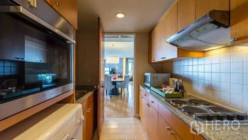 Condominium for rent in Bang Kho Laem, Bangkok - Galley kitchen with cooktop, range hood, microwave and tiled backsplash.
