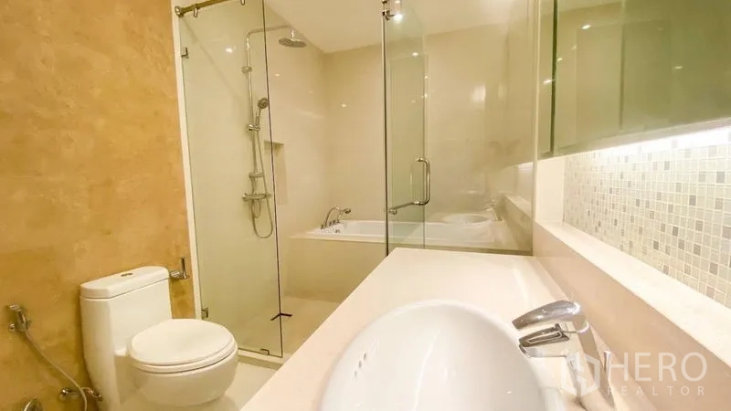 Condominium for rent in Khlong Toei, Bangkok - Bright bathroom with a glass shower, separate bathtub, white vanity and modern fixtures.