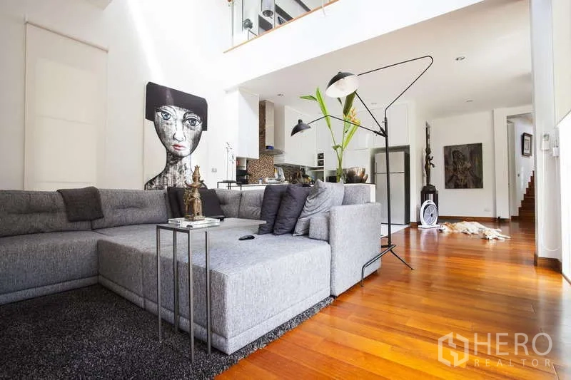 Detached House for rent in Lat Phrao, Bangkok - Cozy lounge with a gray sectional sofa, high ceiling, and a view toward the modern kitchen.