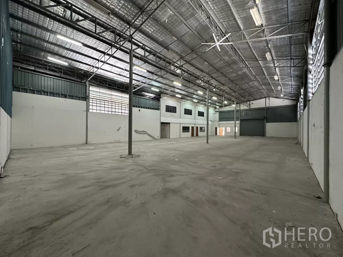 Warehouse for rent in Suan Luang, Bangkok - Wide industrial storage hall with smooth concrete slab, multiple support columns, and a large roller shutter door.