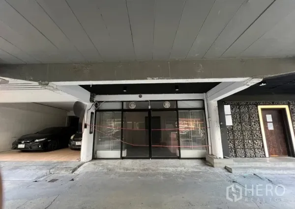 Shophouse for rent in Watthana, Bangkok - Ground-floor shophouse frontage with black-framed glass doors under a covered parking bay.