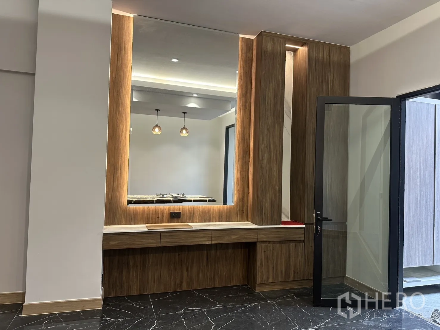 家庭办公室 for rent in Watthana, Bangkok - 木质饰面与大型背光镜面的内置墙面，旁有玻璃门。