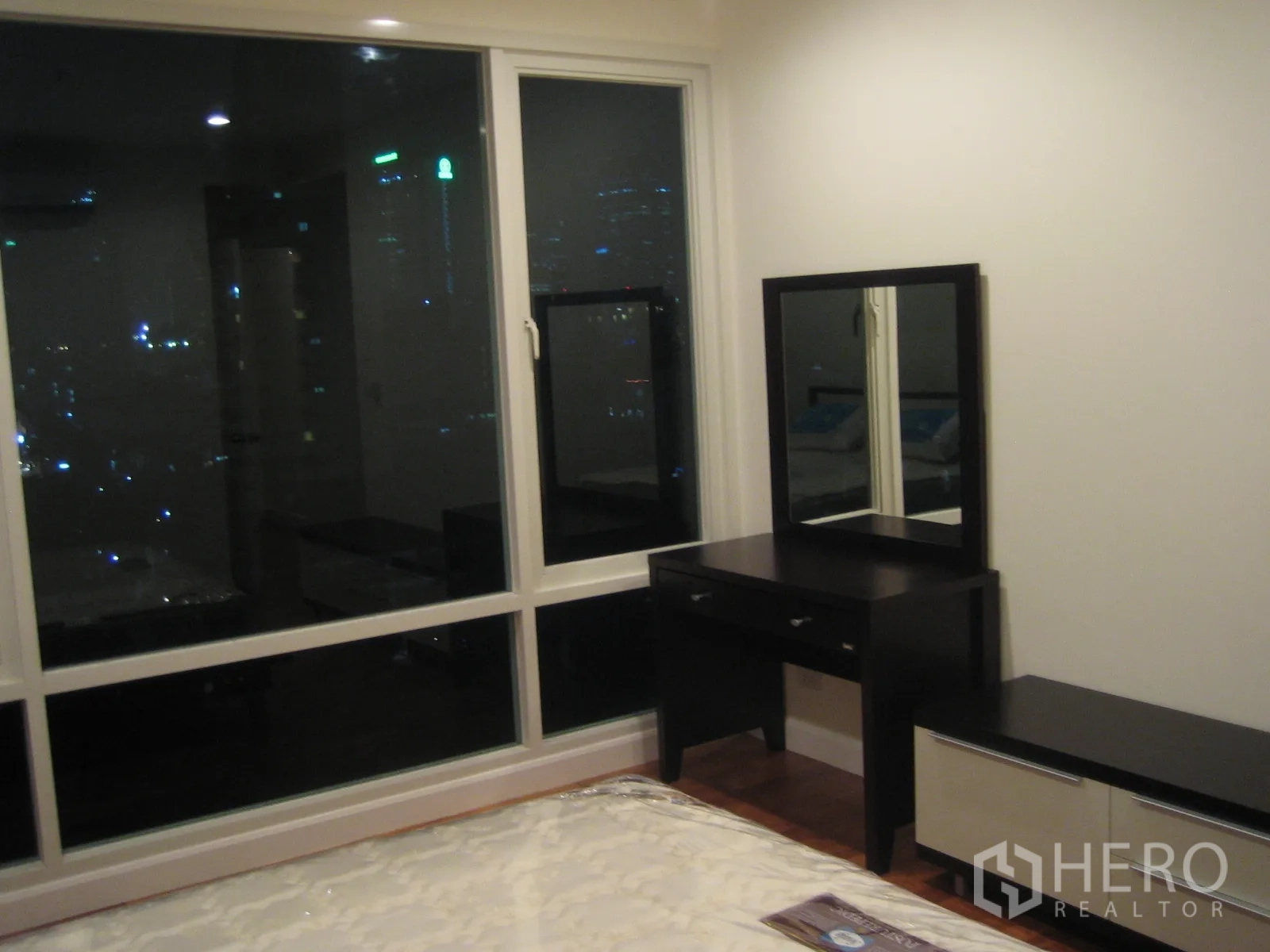 Condominium for rent or sale in Watthana, Bangkok - Bedroom corner with vanity desk and wide city-view windows showcasing the night skyline.
