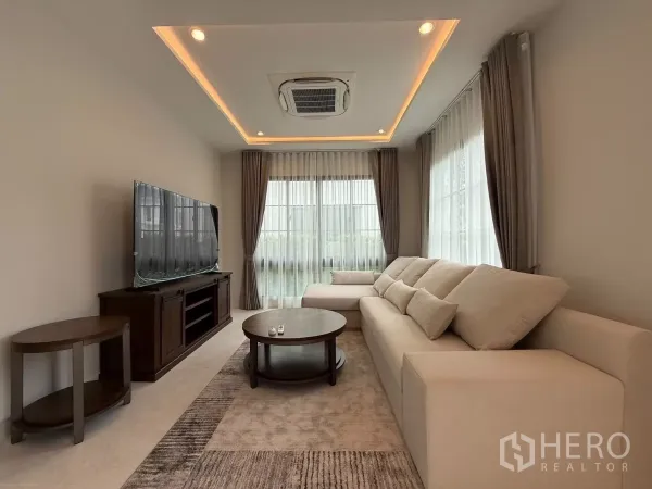 บ้าน ให้เช่าหรือขายในBang Phli, Samut Prakan - ห้องนั่งเล่นสว่างด้วยโซฟาเข้ามุมสีครีม ตู้ทีวี ไฟซ่อนฝ้าพร้อมผ้าม่านโปร่ง