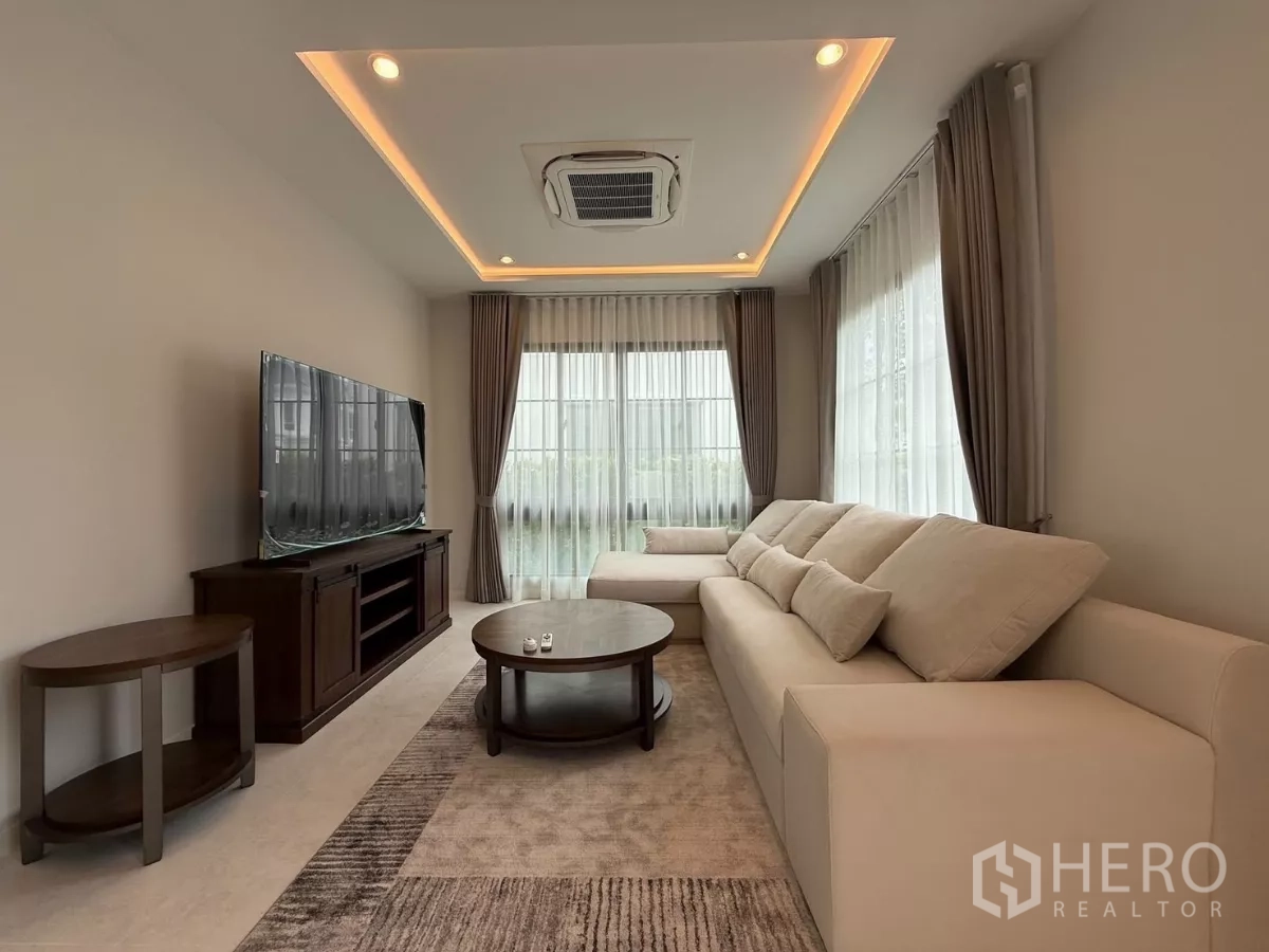 บ้าน ให้เช่าหรือขายในBang Phli, Samut Prakan - ห้องนั่งเล่นสว่างด้วยโซฟาเข้ามุมสีครีม ตู้ทีวี ไฟซ่อนฝ้าพร้อมผ้าม่านโปร่ง