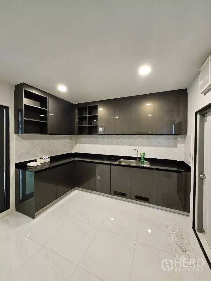 Detached House for rent or sale in Bang Phli, Samut Prakan - Separate Thai kitchen with L‑shaped glossy cabinets, black countertops, and stainless sink.