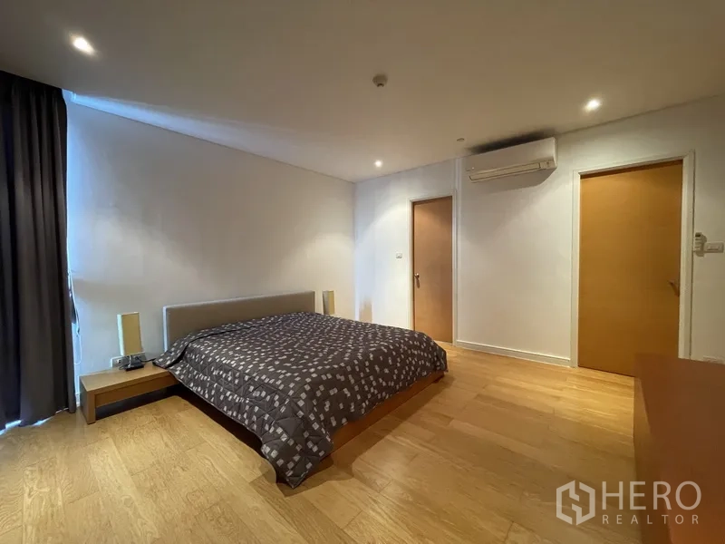 Condominium for rent or sale in Watthana, Bangkok - Spacious primary bedroom with king bed, wood floors, air conditioning, and doors to closet and ensuite.