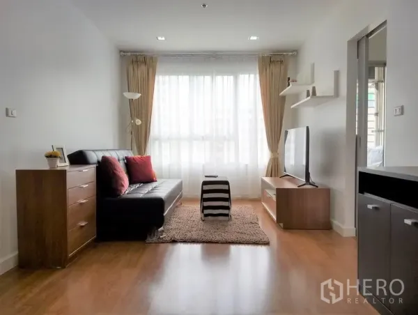 Condominium for rent or sale in Khlong Toei, Bangkok - Bright living room with black leather sofa, TV console, wood flooring and large curtained window.