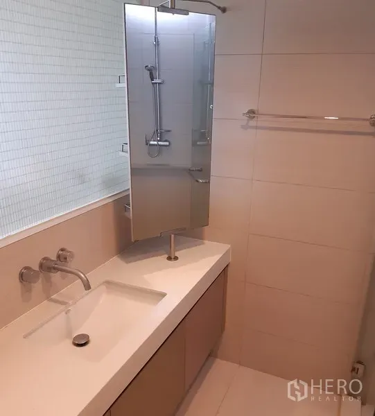 Condominium for rent in Khlong Toei, Bangkok - Contemporary bathroom featuring a long vanity, wall-mounted faucet and glass-enclosed shower.