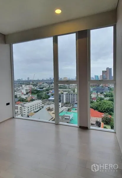 Condominium for sale in Khlong Toei, Bangkok - Bedroom with tall windows showcasing a wide city view and abundant natural light.