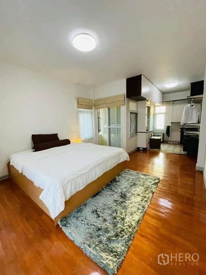 Detached House for rent or sale in Lam Luk Ka, Pathum Thani - Large bedroom with big bed, windows and long shaggy rug on wooden floor.