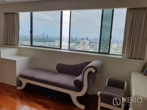 Condominium for rent in Khlong Toei, Bangkok - Cozy chaise lounge beside wide windows showcasing a panoramic Bangkok skyline view.