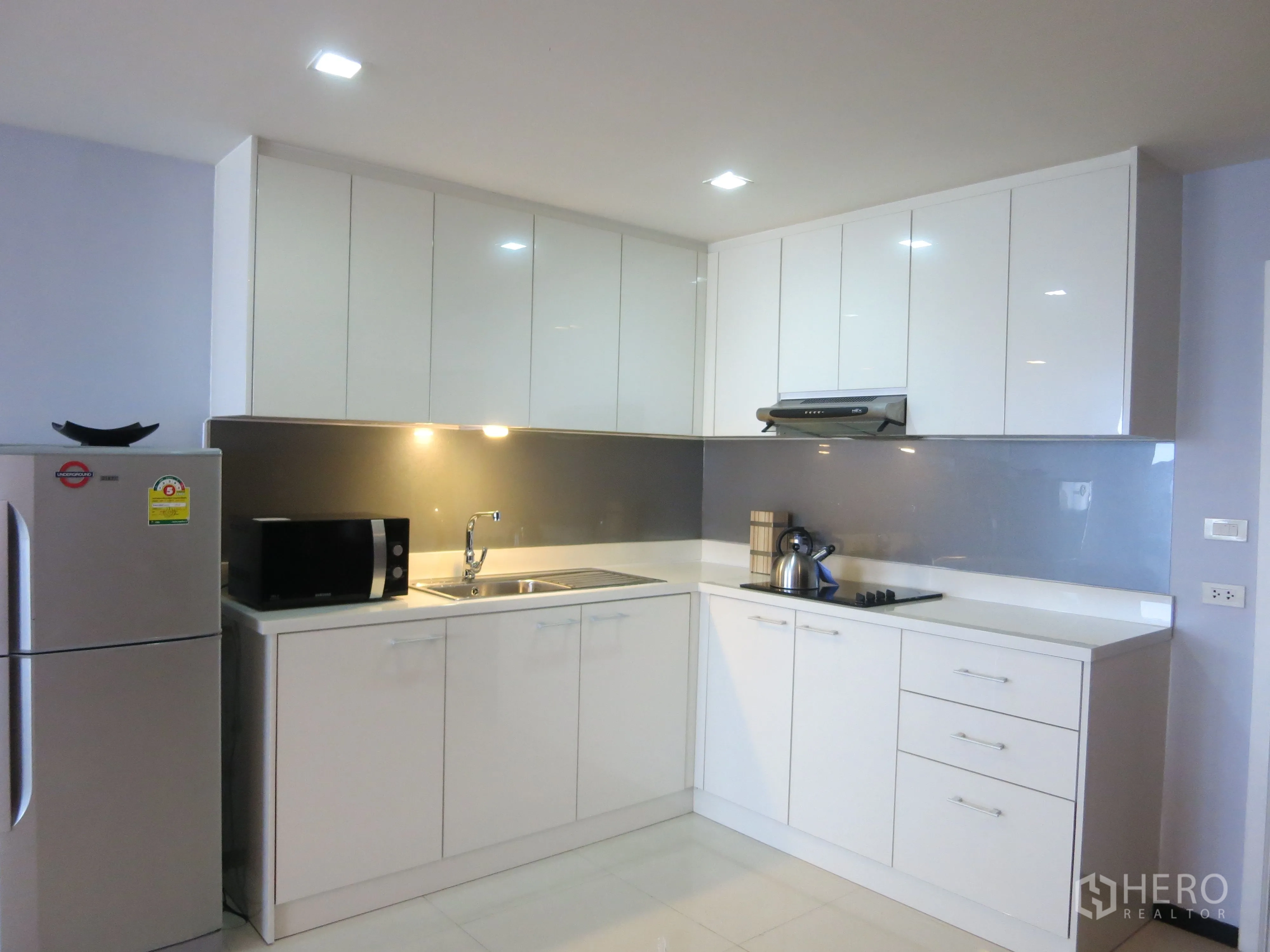 公寓 出租或出售在Watthana, Bangkok - 白色L形整体厨房，充足的柜体、灶台与双门冰箱。