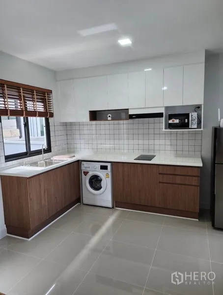 Townhouse for rent in Bang Phli, Samut Prakan - L-shaped kitchen with white cabinets, wood accents, tiled backsplash, stove, fridge, and washer.