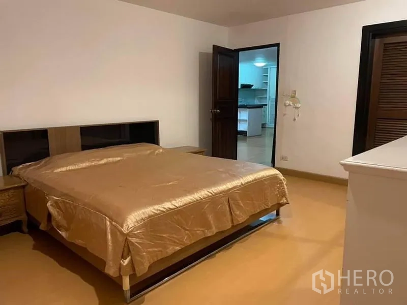 公寓 出租或出售在Watthana, Bangkok - 宽敞卧室，棕色床品、床头柜，门通向起居区。