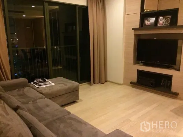 Condominium for rent in Watthana, Bangkok - Living room with sectional sofa, TV wall unit, and sliding glass door to a balcony.