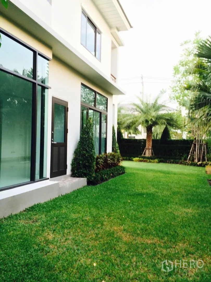 Detached House for sale in Lat Krabang, Bangkok - Side view of a modern two-storey detached house with large windows and a manicured lawn.