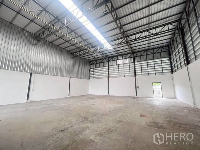 Warehouse for rent in Lam Luk Ka, Pathum Thani - Warehouse interior with high metal truss roof, skylight, and concrete floor.
