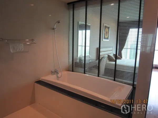 Condominium for rent or sale in Pathum Wan, Bangkok - Bathtub with handheld shower next to window with blinds looking into the bedroom.