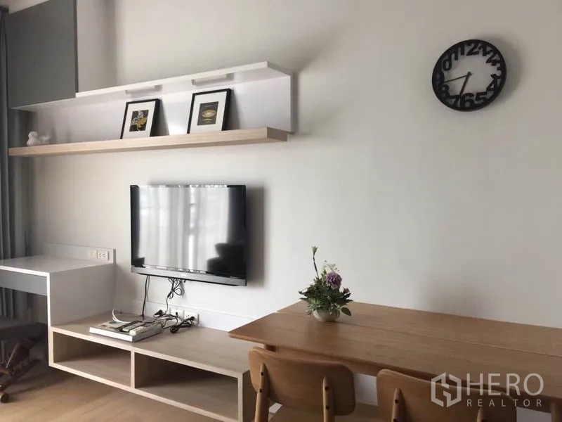 Condominium for rent or sale in Bangkok - Minimalist media wall with floating shelf, TV console, wall clock and a two-seater dining table.