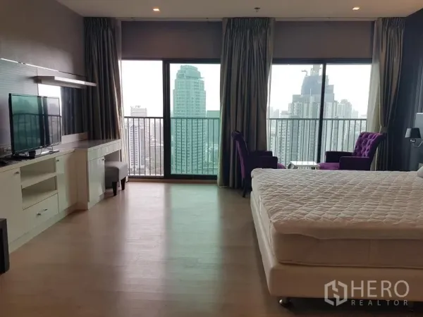 Condominium for rent in Khlong Toei, Bangkok - Large master bedroom with floor-to-ceiling windows, balcony, city view and lounge chairs.
