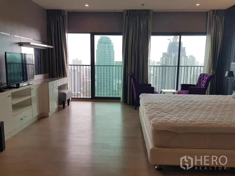 Condominium for rent in Khlong Toei, Bangkok - Large master bedroom with floor-to-ceiling windows, balcony, city view and lounge chairs.