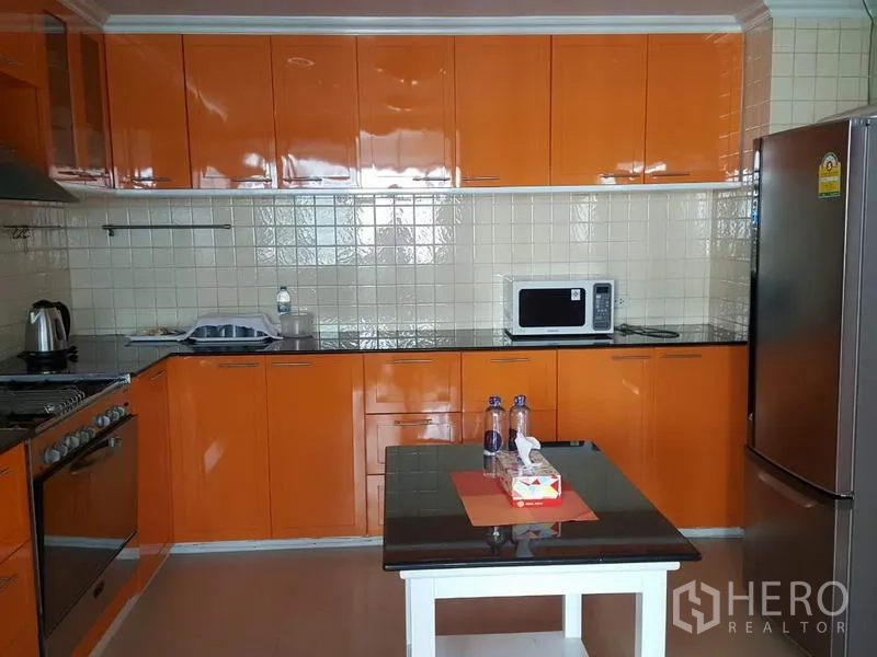 公寓 出租在Watthana, Bangkok - 现代厨房，亮橙色橱柜，瓷砖挡板，小岛台与不锈钢家电。