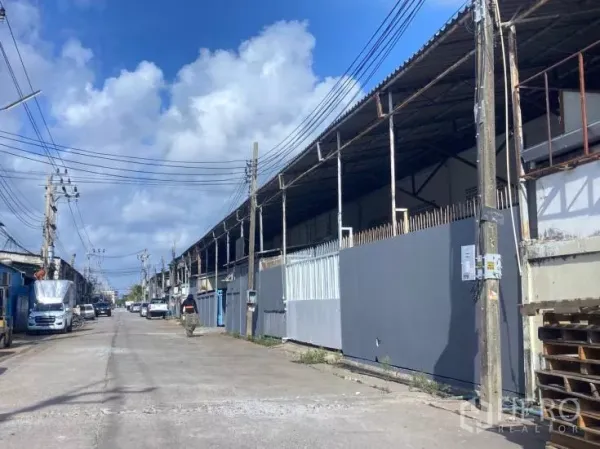 Factory for rent in Bang Phli, Samut Prakan - Row of warehouse buildings along an industrial street with power lines and gated fronts under a blue sky.