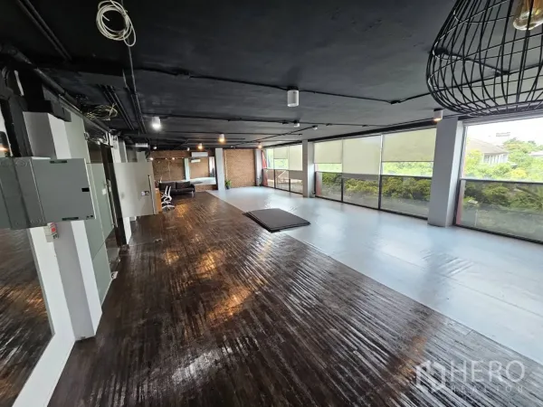 办公空间 出租在Watthana, Bangkok - 宽敞工作区，整排窗户临绿景，深色木地板与工业风黑色天花。