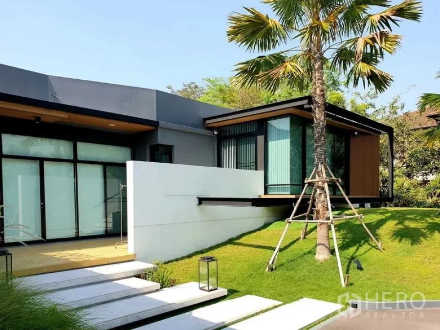 Detached House for rent or sale in Lam Luk Ka, Pathum Thani - Modern facade with white stepping path and a cantilevered glass room above a palm-lined lawn.