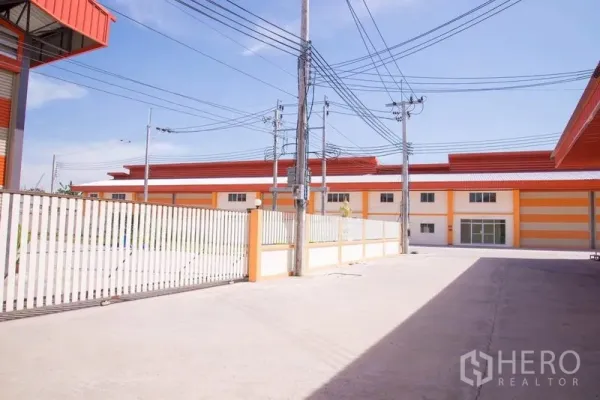 工厂 出售在Mueang Samut Prakan, Samut Prakan - 工业园区封闭式混凝土地面与围栏，可见相邻工厂建筑。