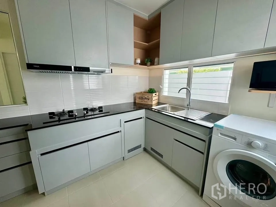 Detached House for rent in Bang Phli, Samut Prakan - L-shaped kitchen featuring black countertops, gas hob, and ample storage.