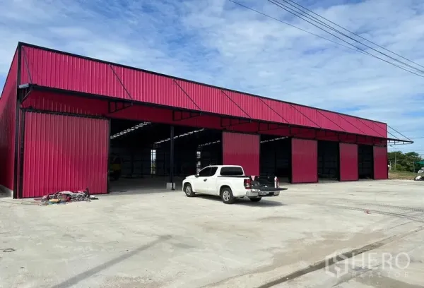 Warehouse for rent in Ban Pho, Chachoengsao - Exterior perspective of the red metal warehouse blocks with spacious concrete yard for truck parking.